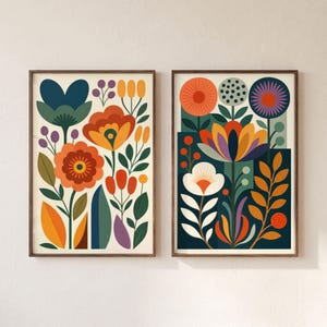 May include: Two rectangular wall art prints featuring stylized floral arrangements. The left print displays orange, yellow, and dark blue flowers on a cream background. The right print shows orange, purple, and white flowers on a dark blue background.