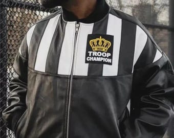 May include: A black and white striped leather bomber jacket with a full-length front zipper and a black ribbed collar. A rectangular patch on the left chest features a gold crown graphic above the text TROOP CHAMPION in white lettering.