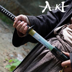 May include: A katana sword with a black handle and a light blue blade. The sword has a gold-colored guard and a black scabbard. The image includes the text "Aki" in Japanese characters.