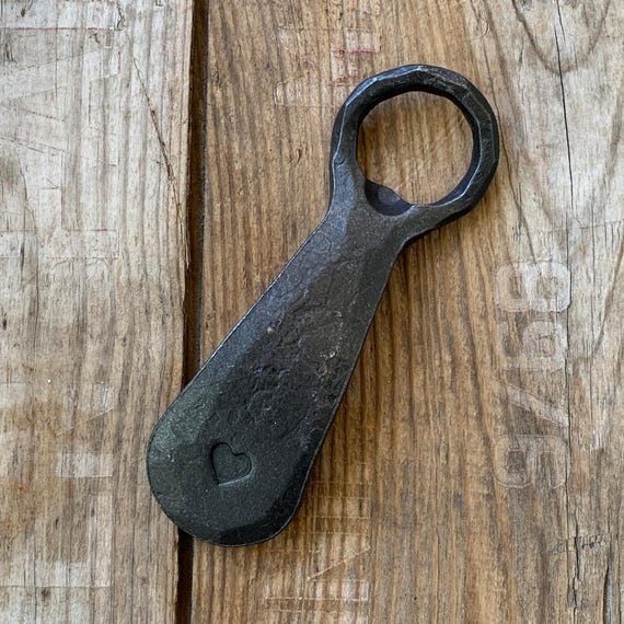 A bottle opener actually hammered into shape at a forge — you can see the hammer marks, and it opens beers with the satisfying heft of real blacksmithed steel.