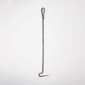 May include: A dark grey, hand-forged fireplace poker with a loop handle and a curved end. The metal poker has a simple, functional design, ideal for tending to a fire. The poker is made of iron and is a useful tool for any fireplace.