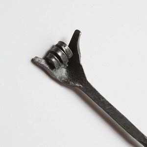 May include: A dark metal wrench shaped like a hand making the "shaka" gesture. The thumb and little finger are extended. The wrench is set against a plain white background.