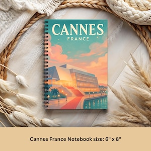 May include: Spiral-bound notebook featuring a colorful illustration of Cannes, France, with the text "Cannes France." The cover art depicts a modern building with a red carpet and water. The notebook measures 6" x 8".