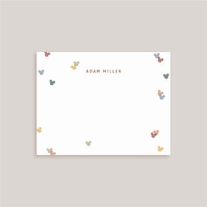 May include: A white rectangular stationery card featuring the name ADAM MILLER printed in brown text at the top center. The card is decorated with a scattered pattern of small, muted-colored mouse-shaped icons in shades of blue, green, and tan.