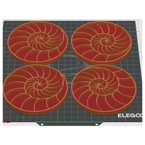 Puede incluir: Cuatro posavasos redondos con un dise&ntilde;o de concha de nautilus. Los posavasos son de color marr&oacute;n rojizo con un patr&oacute;n en espiral marr&oacute;n claro. Est&aacute;n dispuestos sobre una superficie de rejilla negra.