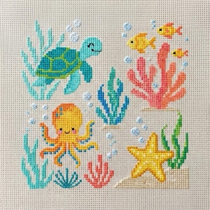 Può includere: Design a punto croce raffigurante una scena sottomarina. Una tartaruga turchese nuota sopra un polpo giallo, con pesci gialli, coralli e una stella marina. Alghe blu e verdi e bolle completano il tema oceanico, il tutto cucito su uno sfondo neutro.