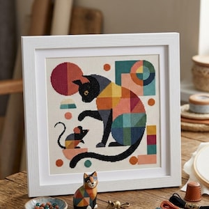 May include: A framed cross-stitch embroidery featuring a geometric cat and mouse design. The cat is composed of multicoloured squares in shades of blue, yellow, orange, and red. A small mouse sits before the cat, also rendered in geometric shapes.