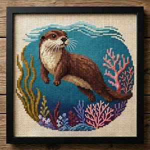 May include: Framed cross-stitch art depicting a brown otter in a blue underwater scene. The artwork includes coral, seaweed, and water details. The otter has a light brown chest and a dark brown body. The frame is black.