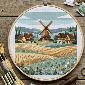 May include: A completed cross-stitch landscape scene featuring a windmill, houses, and fields of wheat. The artwork is framed in a wooden embroidery hoop. The color palette includes shades of beige, brown, green, and blue, creating a pastoral scene.
