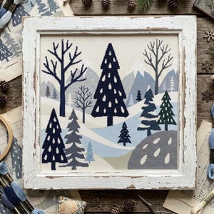 May include: A square cross-stitch embroidery featuring a winter landscape with dark blue and grey pine trees, bare trees, and snow-covered mountains. The artwork is displayed in a distressed white wooden frame with a visible grain texture.