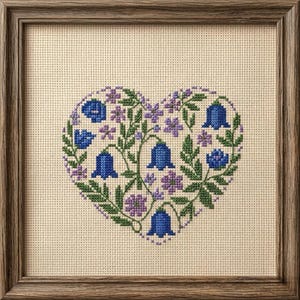 May include: Cross-stitch artwork of a heart shape, framed in wood. The heart is filled with bluebell flowers, green leaves, and purple flowers. The background is a light beige fabric.