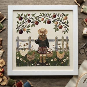 May include: A framed cross-stitch embroidery depicting a person in a straw hat, dark jacket, and patterned skirt standing before a wooden fence. The scene includes an apple tree with red and yellow fruit, a small basket, and three chickens.