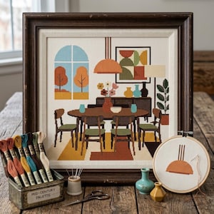 Può includere: Un ricamo a punto croce incorniciato che raffigura una sala da pranzo con un tavolo ovale, sedie e una finestra con vista su alberi autunnali. Accanto si trova una scatola di metallo con etichetta Mid-Century Palette, filati, un telaio e due vasi.