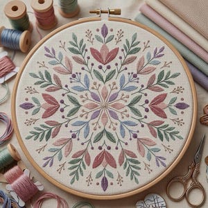 Może przedstawiać: Ukończony projekt haftu krzyżykowego z kwiatowym wzorem w drewnianym tamborku. Wzór zawiera liście, jagody i kształty kwiatów w odcieniach różu, zieleni i błękitu. Szpulki nici i tkanina w tle.