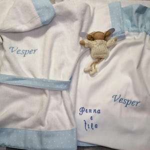 May include: White terry cloth robe and matching garment with light blue polka dot trim. The name "Vesper" is embroidered in blue on the robe and garment. A small doll with wings is also present.
