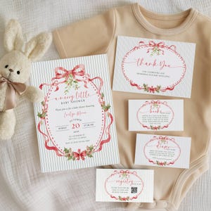 May include: A beige baby bodysuit, a plush rabbit toy, and a set of baby shower stationery featuring a red ribbon and holly design. The cards include text for a baby shower invitation, a thank you note, a book request, a diaper raffle, and a registry.