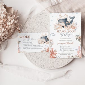 K&ouml;nnte beinhalten: Babyparty-Einladungen und Karten zur Buchanforderung. Die Einladung zeigt eine Illustration eines Delfins, Muscheln und florale Akzente. Die Karte enth&auml;lt den Text "Sea You Soon Baby" und Veranstaltungsdetails.