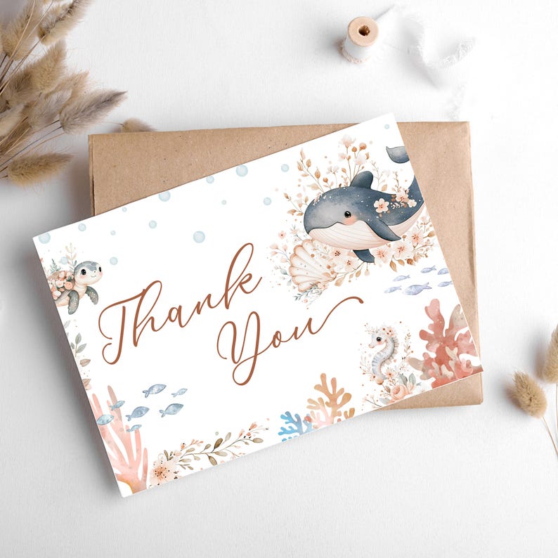 K&ouml;nnte beinhalten: Eine wei&szlig;e Karte mit einer Aquarellillustration eines Wals, einer Meeresschildkr&ouml;te und eines Seepferdchens, umgeben von Korallen und Blumen. Die Worte "Thank You" sind in brauner Schrift geschrieben. Die Karte liegt auf einem braunen Umschlag.