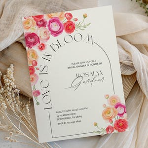 May include: A cream-coloured invitation with floral accents. The text "Love is in Bloom" and "Please join us for a bridal shower in honour of Rosalyn Gardner" is displayed. The invitation includes the date, time, and location.