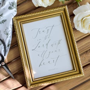 May include: A gold framed print with the text "Trust in the Lord with all your heart" and the scripture reference "Proverbs 3:5".