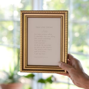 May include: A framed print with a gold frame and a white background. The print features a pink text quote about hope and faith. The quote reads "This One Thing" and includes the verse "Lamentations 3:21-24".