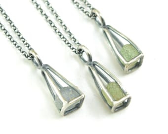 May include: Three silver necklaces with a small, clear glass pendant containing a green stone. Each pendant is shaped like a pyramid with a square base.
