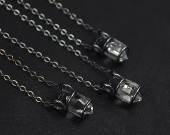 May include: Three silver chains with clear crystal pendants hanging from them. The crystals are encased in a silver cage.