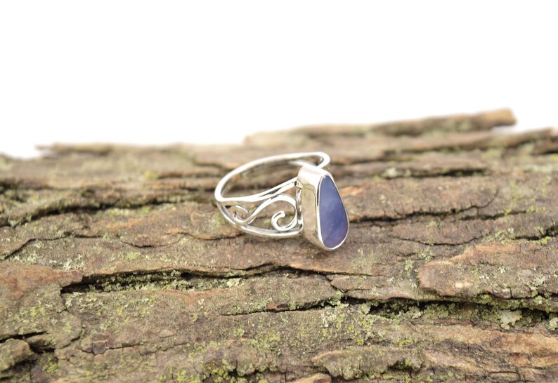 May include: A silver ring with a teardrop-shaped purple gemstone set in a delicate, swirling design.