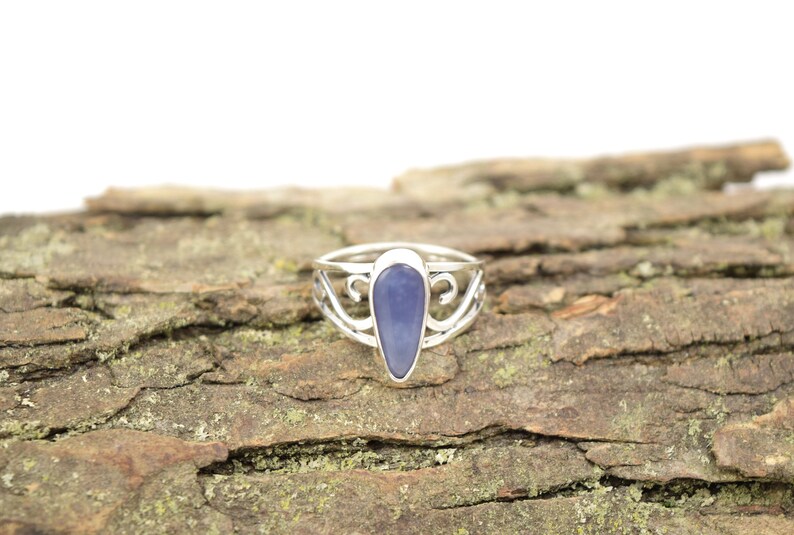 May include: A silver ring with a teardrop-shaped blue gemstone set in a delicate, swirling design.