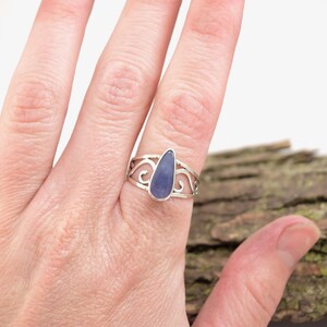 May include: A silver ring with a teardrop-shaped blue gemstone set in a delicate, swirling design.