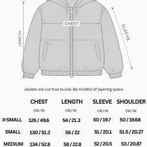 May include: Diagram of a boxy drop shoulder jacket with measurements in inches and centimeters. The diagram shows chest, length, sleeve, and shoulder dimensions for sizes X-Small to 2X-Large. The jacket has a hood and a full-length zipper.
