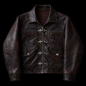 May include: A brown leather jacket with a collared neckline and a zipper closure. The jacket features four silver metal clasps and two front pockets with button closures. The jacket has a worn, distressed appearance.