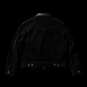 May include: Black denim jacket with a leather collar, viewed from the back. The jacket features silver buttons and a classic design. The dark wash denim gives it a vintage look. A stylish piece for any wardrobe.