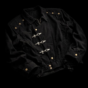 May include: A black jacket featuring a fold-down collar, long sleeves with buttoned cuffs, and a front closure with three silver-toned metal toggle clasps. The garment is accented with small gold-toned metal studs along the shoulders and hem.