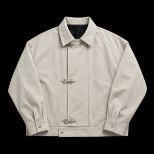 Könnte beinhalten: Eine hellbeige Jacke mit spitzem Kragen, langen Ärmeln mit geknöpften Manschetten und einer Vorderseite, die mit drei silberfarbenen Knebelverschlüssen aus Metall geschlossen wird. Das Innenfutter ist schwarz und der Schnitt ist strukturiert.