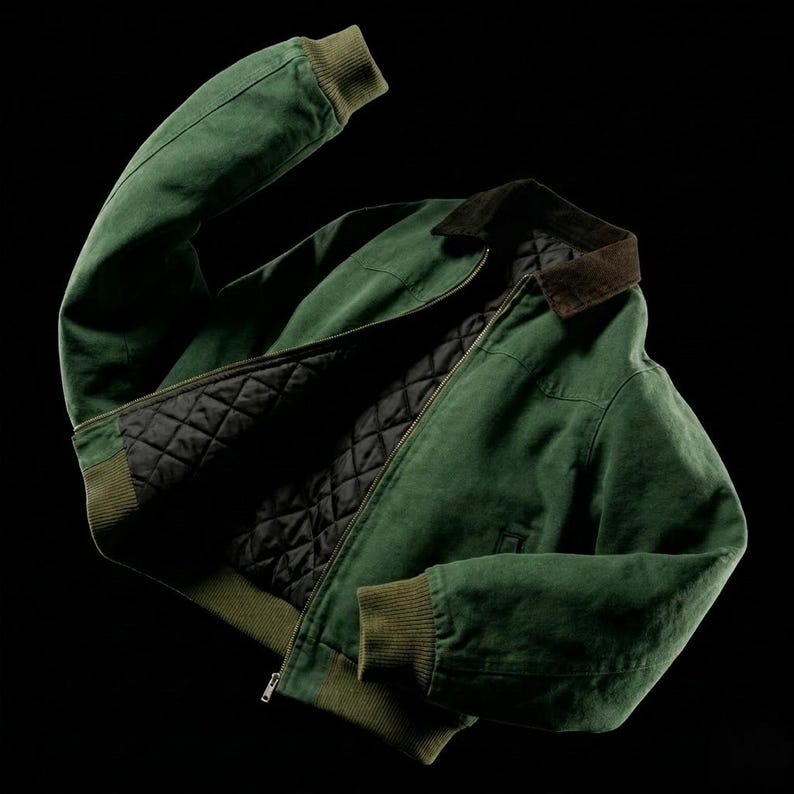 May include: A green bomber jacket with a brown collar and a black quilted lining. The jacket has ribbed cuffs and hem in a matching green color. The zipper is silver. The jacket is displayed against a black background.