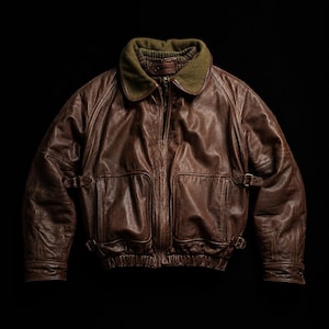 Peut inclure: Un blouson aviateur en cuir marron avec une finition texturée, un col en laine vert olive foncé et une fermeture éclair centrale. La veste comprend deux grandes poches avant, des sangles à boucle latérales réglables, ainsi que des poignets et un ourlet côtelés.