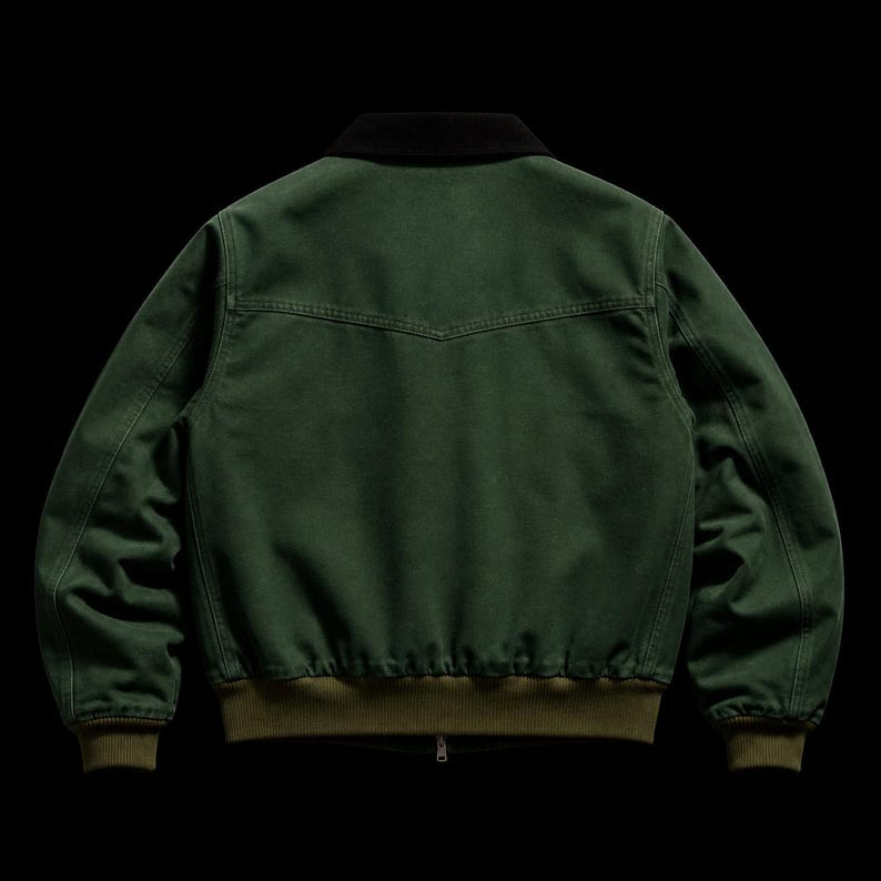 May include: A dark green bomber jacket with a black collar and a zipper closure. The jacket has a ribbed olive green hem and cuffs. The back of the jacket features a yoke detail. The jacket is made of a durable fabric.