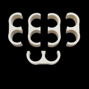 May include: Off-white, semi-circular plastic clips arranged against a black background. The clips have a smooth, matte finish and are designed with a curved shape, suggesting they are for holding or securing items.
