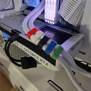 May include: Close-up of a computer's internal components, featuring white cables secured with colorful clips. The text "GEFORCE RTX" is visible on a component. The clips are red, white, black, blue, and green.