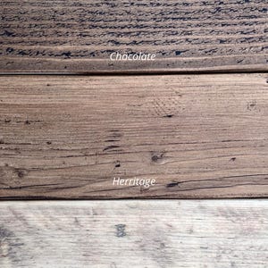 Op de afbeelding: Close-up van drie houten planken met verschillende afwerkingen. De bovenste plank is donker chocoladebruin, de middelste plank is bruin en de onderste plank is licht en natuurlijk van kleur. De tekst "Chocolate", "Herritage" en "Natural" is zichtbaar.