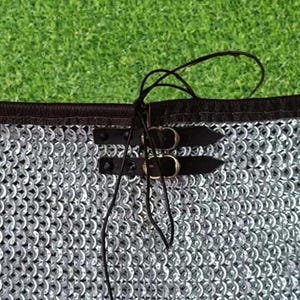 Puede incluir: Primer plano de una prenda de cota de malla con ribete negro y correas de cuero con hebillas. La cota de malla est&aacute; hecha de peque&ntilde;os anillos met&aacute;licos entrelazados. La prenda tiene una etiqueta con un emblema rojo, blanco y negro y el texto "VIKING CHAINMAIL USA".