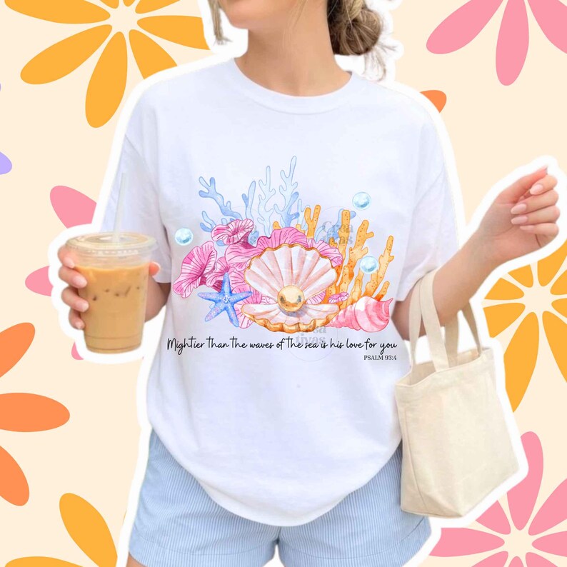 May include: A white t-shirt featuring a colorful graphic of a seashell with a pearl, blue starfish, coral, and bubbles. The text reads, Mightier Than The waves of The sea is his love for you PSALM 93:4. The shirt has a crew neck and short sleeves.