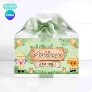 Pode incluir: Caixa de presente branca com uma fita verde e um design com tema de selva. A caixa apresenta o nome "Matheo" e a frase "is turning 2". Personagens de desenhos animados e balões decoram a frente. A caixa está rotulada como "Editable in Canva".