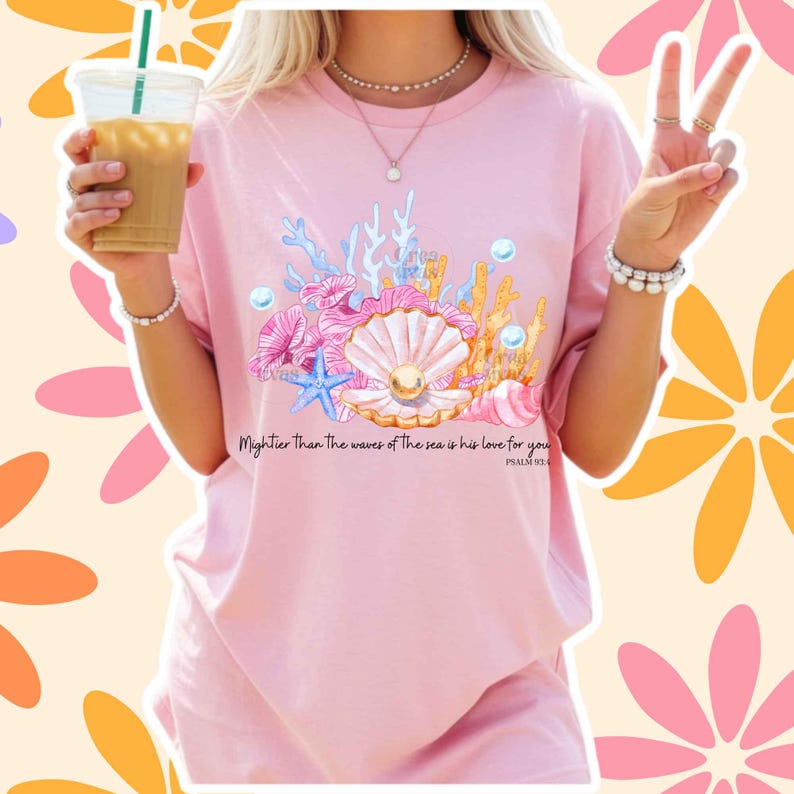 May include: A light pink t-shirt featuring a graphic print of a seashell with a pearl, coral, and a blue starfish. The text "Mightier than the waves of the sea is his love for you" and "PSALM 93:4" is printed in black below the aquatic illustration.