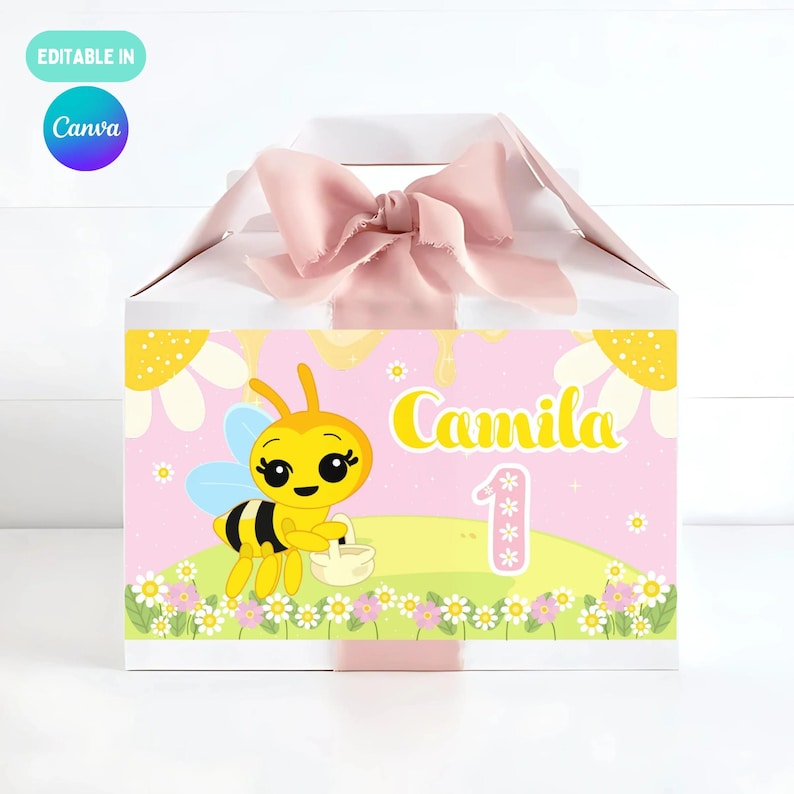 May include: A white gift box with a pink bow. The front displays a cartoon bee, the name "Camila", and the number "1". The design is set against a pink backdrop with floral elements.