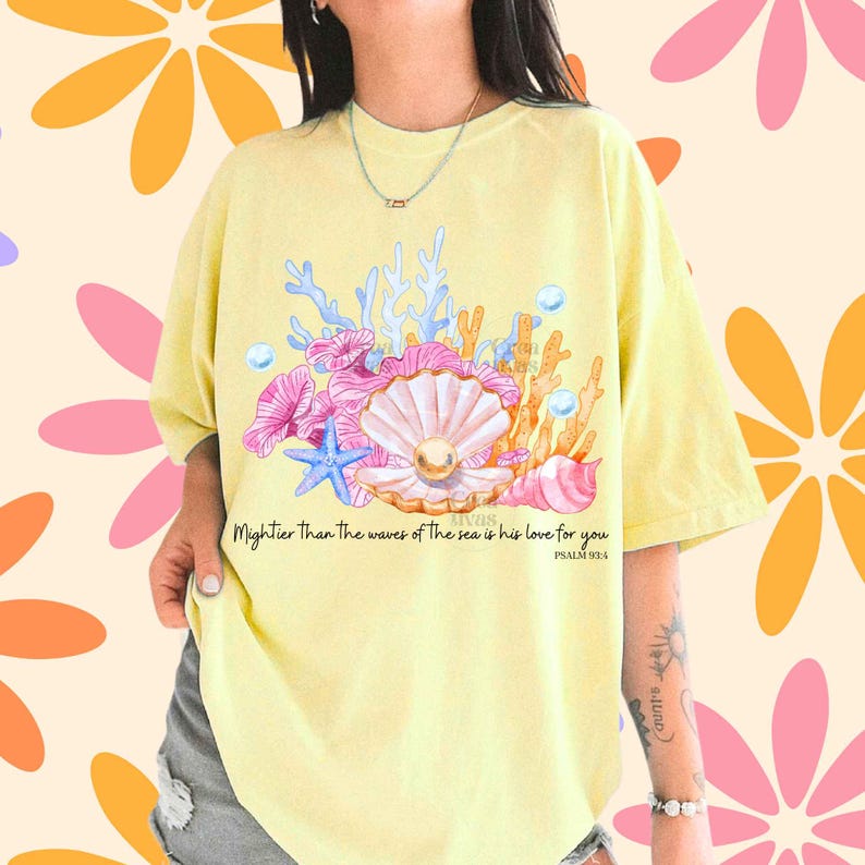 May include: A pale yellow t-shirt featuring a graphic of a pearl inside an open seashell, surrounded by pink and blue coral, a blue starfish, and bubbles. The text reads: Mightier Than The waves of The sea is his love for you PSALM 93:4.