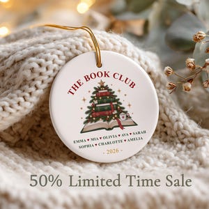 May include: A round white ceramic ornament featuring a graphic of a Christmas tree made of stacked books on an open book. The text reads THE BOOK CLUB, followed by a list of names separated by hearts, and the year 2026 at the bottom in gold.