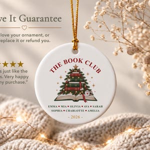 May include: A round white ceramic ornament featuring a gold hanging string. The design displays a stack of books shaped like a Christmas tree, topped with a star. Text reads THE BOOK CLUB, a list of names, and 2026. The graphic includes small stars.