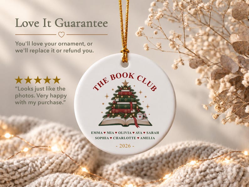 May include: A round white ceramic ornament featuring a gold hanging string. The design displays a stack of books shaped like a Christmas tree, topped with a star. Text reads THE BOOK CLUB, a list of names, and 2026. The graphic includes small stars.